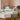 Neatly folded white and sage green polyester tablecloths on a wooden shelf with a wicker laundry basket